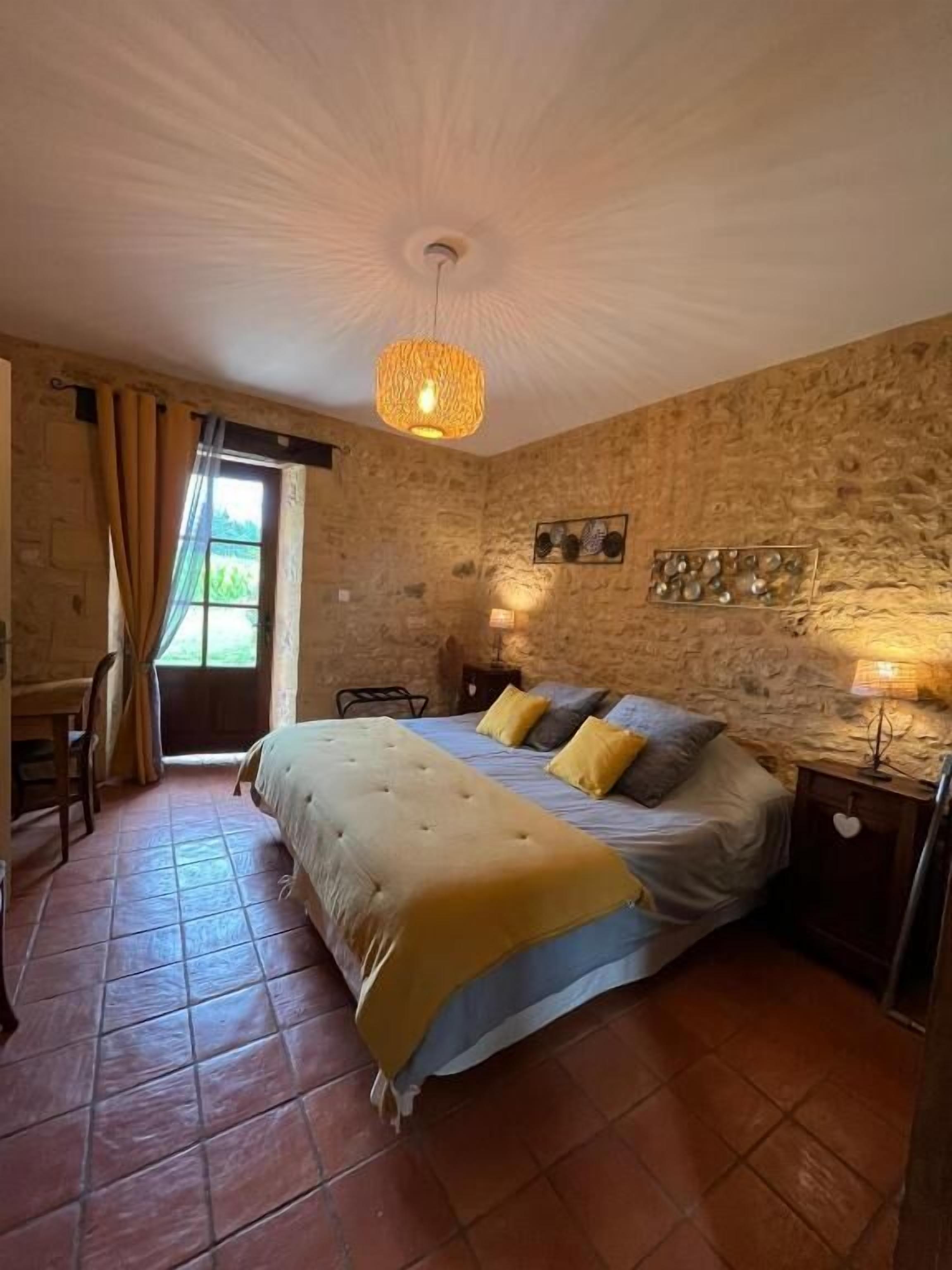 A bedroom with a bed, a chair, a table, and a window with curtains.