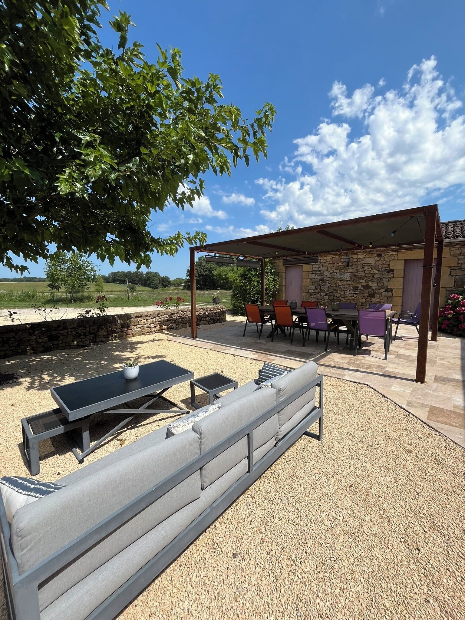 Un patio exterior con muro de piedra, pérgola y zona de estar con mesa y sillas.