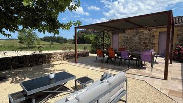 Un patio exterior con muro de piedra, pérgola y zona de estar con mesa y sillas.
