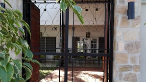 A stone-walled building entrance with a metal gate, a paved patio, and a view of the interior through the gate. - Urban Lodge (Bujumbura)