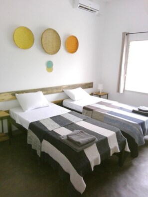 A hotel room with two single beds, a wooden headboard, a small bedside table with a lamp, and a window with curtains. - Urban Lodge (Bujumbura)