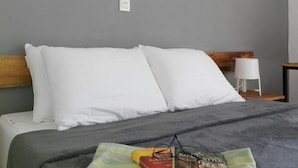 A neatly made bed with white pillows and a grey blanket, a book, and a pair of glasses on a striped pillow. - Urban Lodge (Bujumbura)