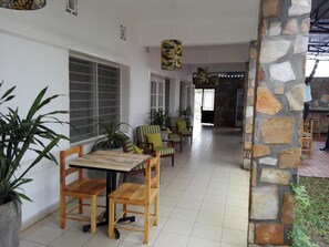 A spacious indoor area with a stone wall, tiled floor, and several wooden chairs and tables. - Urban Lodge (Bujumbura)