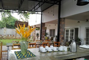 An outdoor dining area with tables set for breakfast, a coffee pot, and a decorative vase with yellow flowers. - Urban Lodge (Bujumbura)