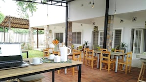 A spacious patio area with wooden tables and chairs, a laptop on a table, and a coffee setup. - Urban Lodge (Bujumbura)
