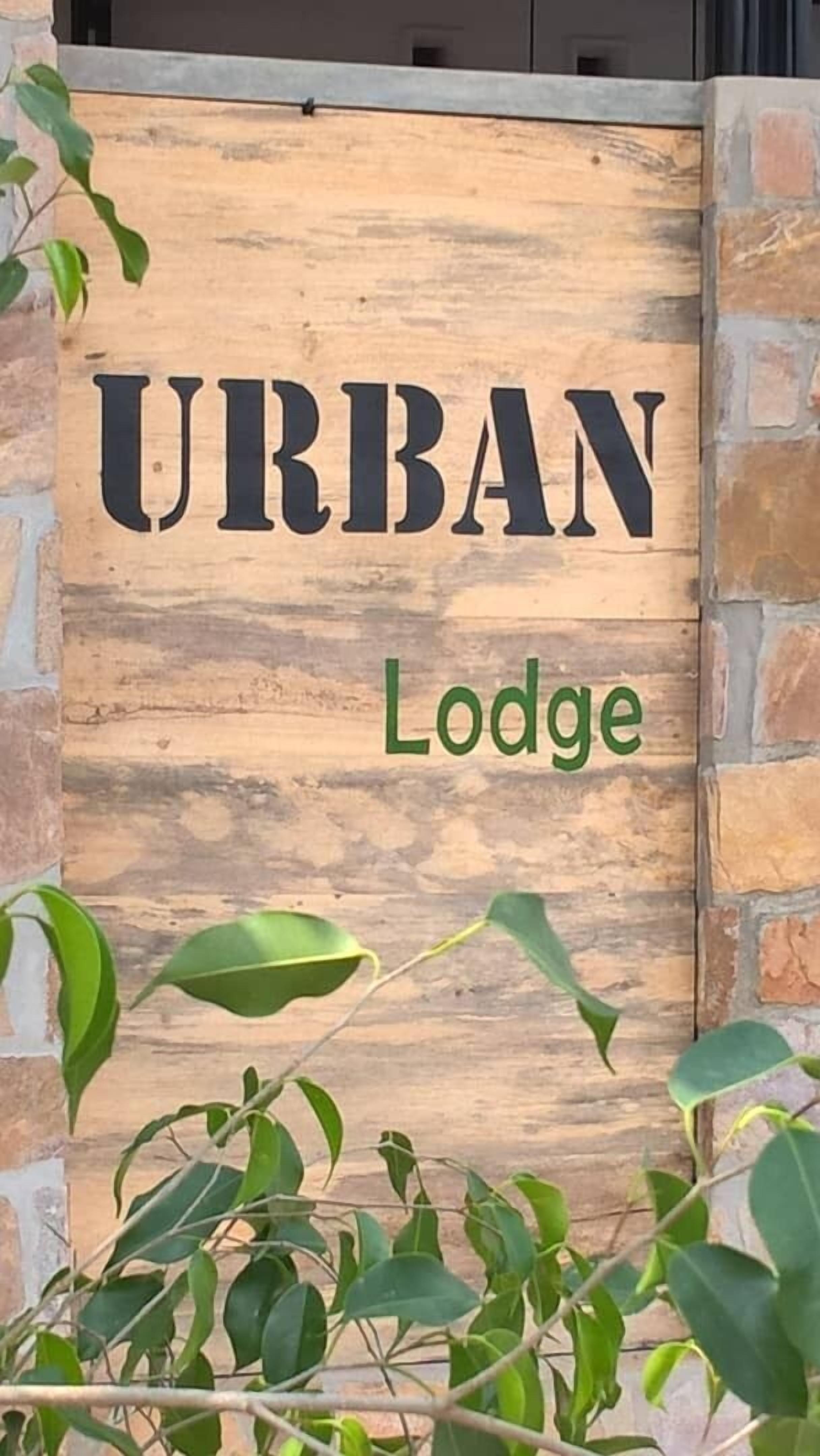 Ein hölzernes Schild mit der Aufschrift 'URBAN Lodge', umgeben von viel Grün.