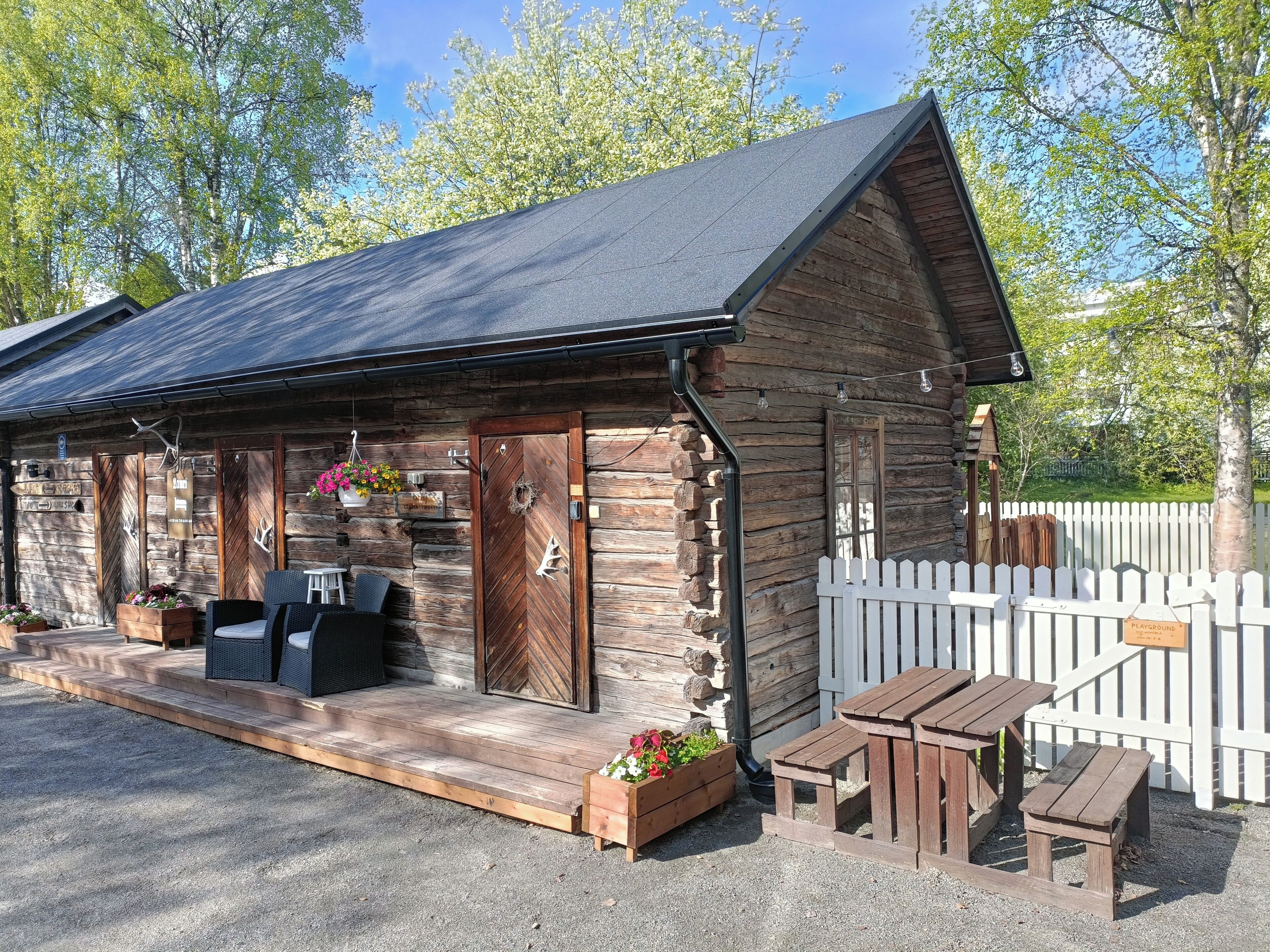 A rustic wooden building with a porch, outdoor seating, and a white picket fence.