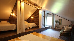 Un dormitorio con techo inclinado, piso de madera, cama con ropa blanca, una mesa con un manual y una silla.