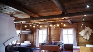 Interior rústico de una cabaña de madera con una cama en el altillo, un sofá y una lámpara colgante.