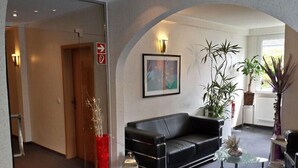 A modern lobby with a black leather sofa, a glass coffee table, and potted plants. - Hotel Merkur Garni (Giesen)
