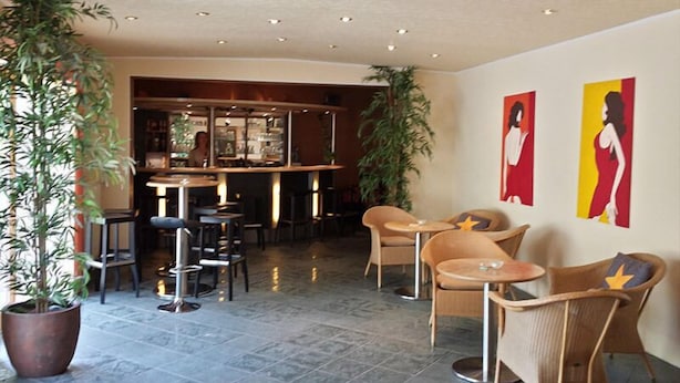 A spacious lobby with a bar area, seating arrangements, and large potted plants. - Hotel Merkur Garni (Giesen)