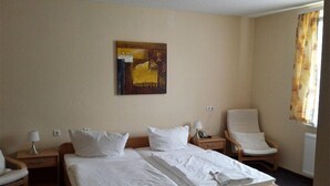 A hotel room with a large bed, two bedside tables, a chair, and a painting on the wall. - Hotel Merkur Garni (Giesen)