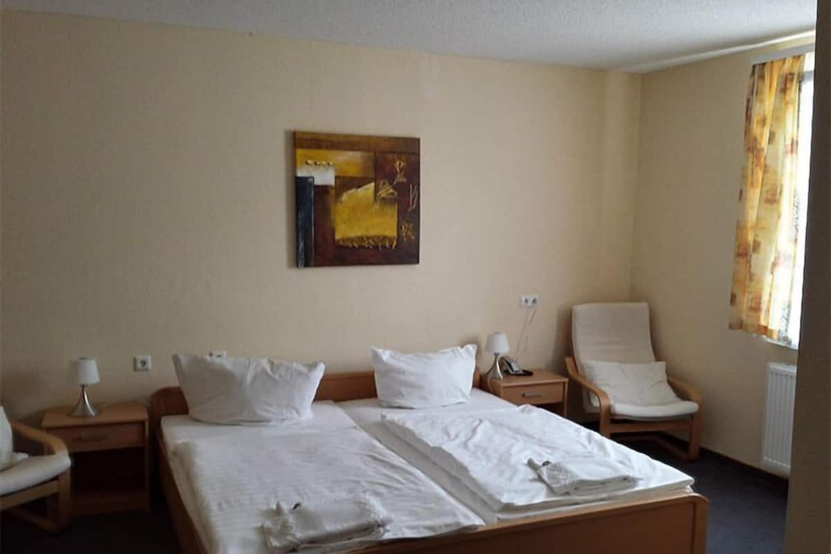 A hotel room with a large bed, two bedside tables, a chair, and a painting on the wall.
