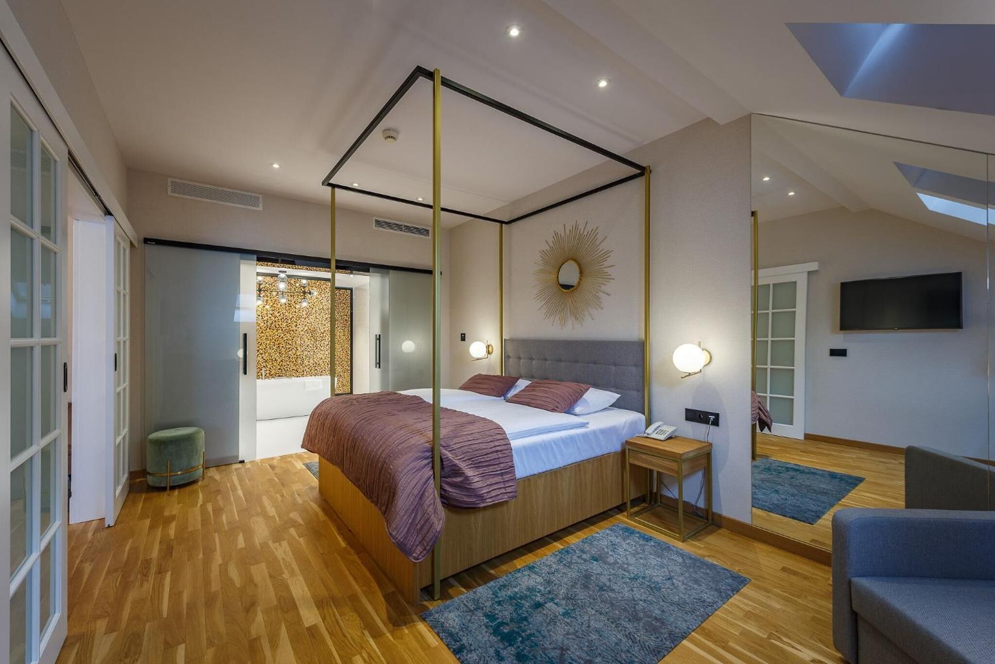 Een moderne slaapkamer met een hemelbed, een grote spiegel en een flatscreen televisie.