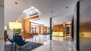 A modern hotel lobby with a spacious area, a reception desk, and a staircase leading to an upper level. - Hotel Prezydent (Inowlodz)