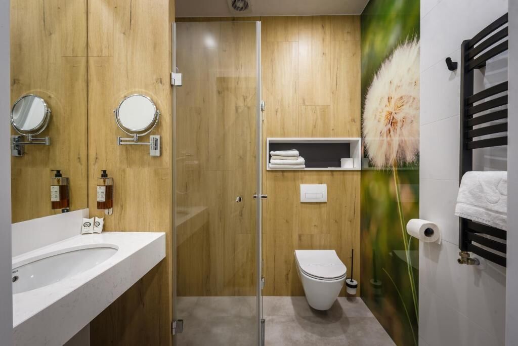 A modern bathroom with a wooden vanity, a glass shower enclosure, a toilet, and a towel rack.