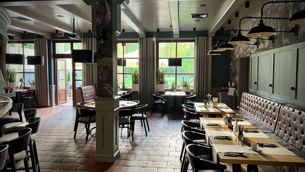 A restaurant with brick flooring, wooden tables, leather booths, and large windows offering a view of greenery. - Hotel Prezydent (Inowlodz)