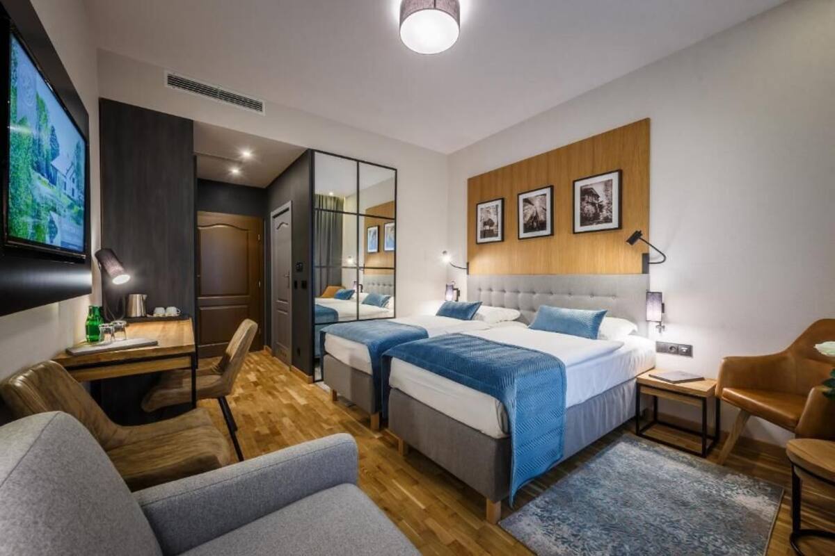 A modern hotel room with two beds, a desk, a TV, and a seating area.