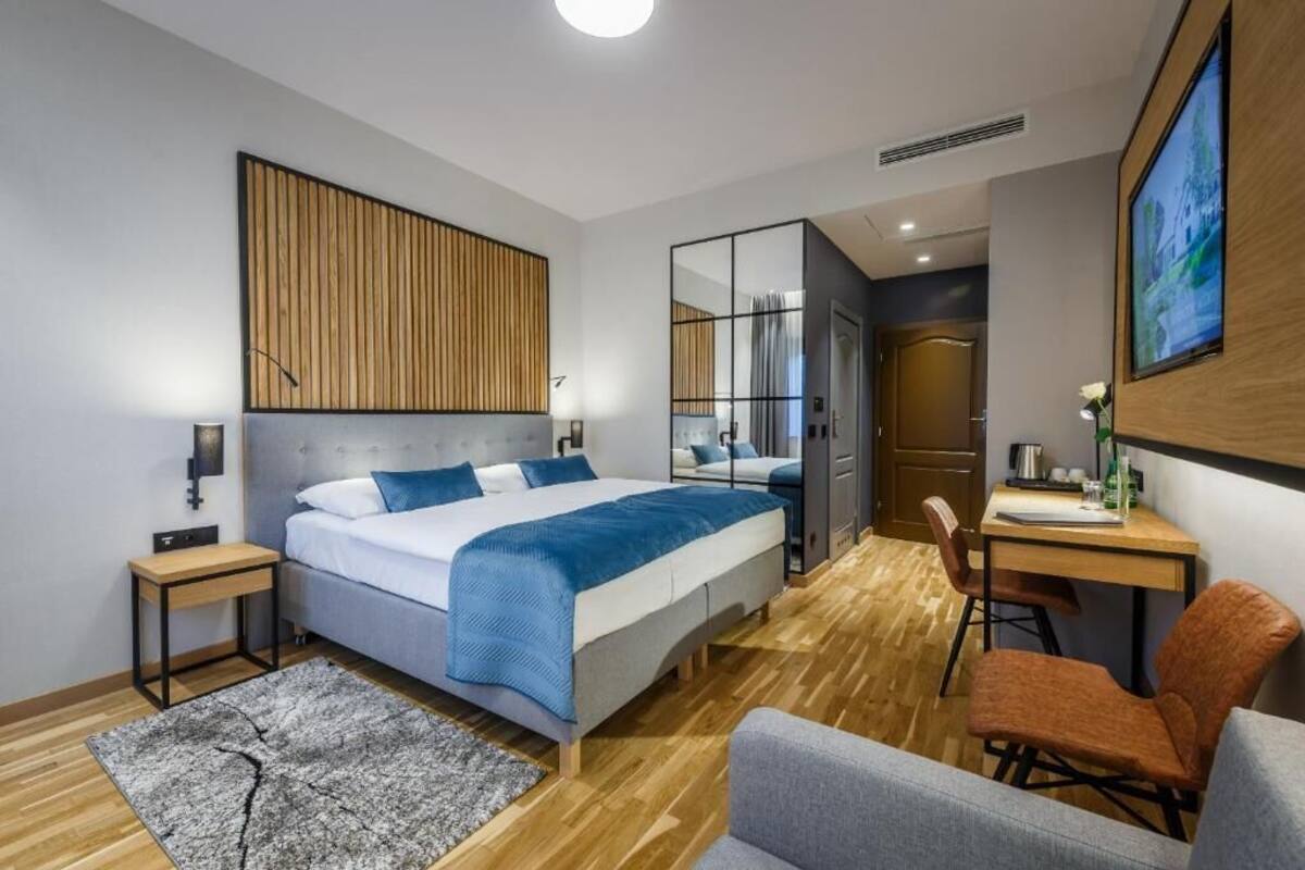 A modern hotel room with a large bed, a desk, a chair, and a mirror.