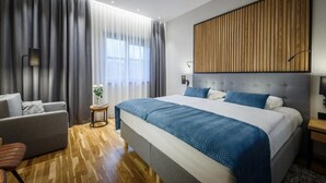 A modern hotel room with a large bed, a sofa, a small side table, and a window with curtains. - Hotel Prezydent (Inowlodz)