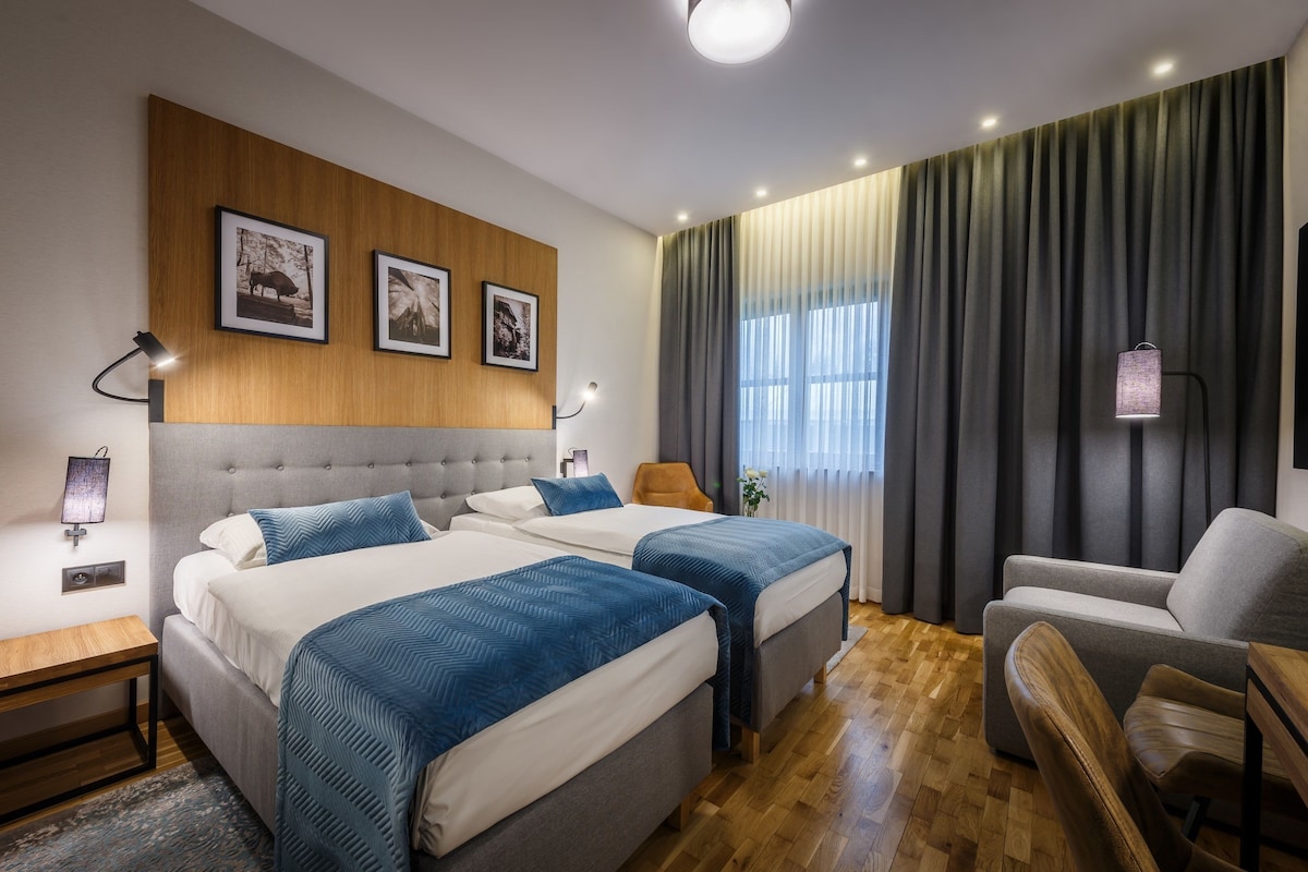 Une chambre d’hôtel avec deux lits, un canapé, une chaise, une tête de lit en bois et une lampe fixée au mur.