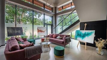 Una sala de estar moderna con ventanas grandes, un sofá rosa, un reposapiés verde y un caballete con una pintura.