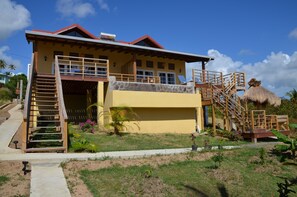 Uma casa de dois andares com telhado vermelho, varanda e estrutura de colmo.