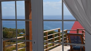A room with large windows offering a view of the ocean and a red-roofed structure. - Kaye Coco (Choiseul)