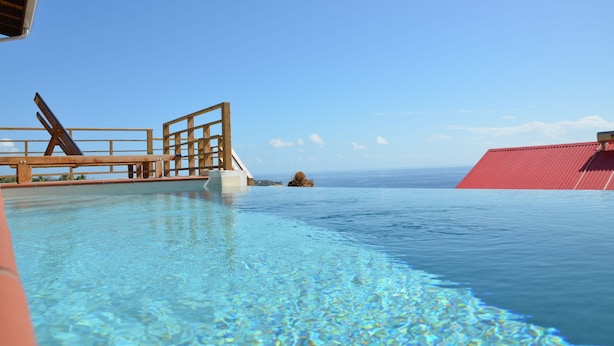 A clear blue pool with a wooden deck and a red building in the background. - Kaye Coco (Choiseul)
