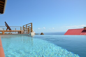 A clear blue pool with a wooden deck and a red building in the background.