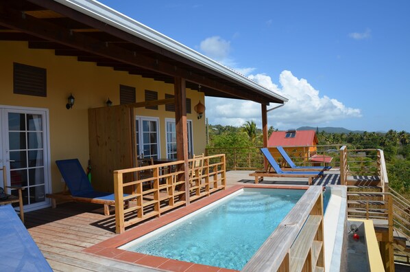 Um deck de madeira com piscina, espreguiçadeiras e área coberta com vista para a paisagem.