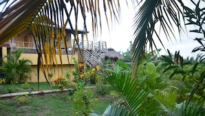 A tropical garden with a thatched-roof structure, a staircase leading to a balcony, and lush greenery. - Kaye Coco (Choiseul)
