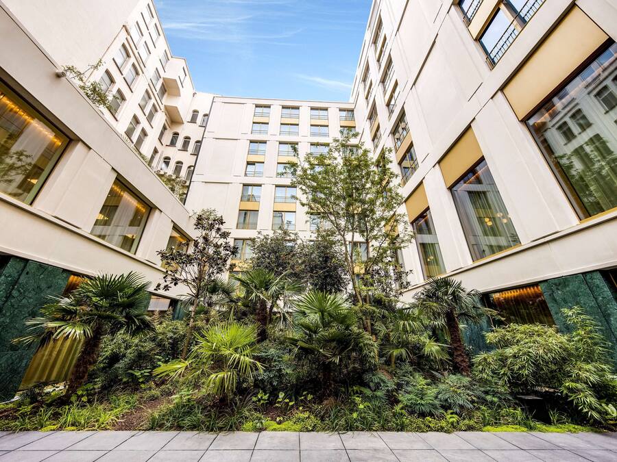 Ein modernes Gebäude mit mehreren Stockwerken, großen Fenstern und einem üppigen Gartenbereich mit verschiedenen Pflanzen und Bäumen.