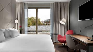 Une chambre d’hôtel dotée d’un grand lit, d’un bureau, d’une chaise, d’une télévision et offrant une vue sur la ville grâce à de grandes fenêtres.