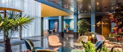 A modern lobby with a glass wall, seating areas, and potted plants.
