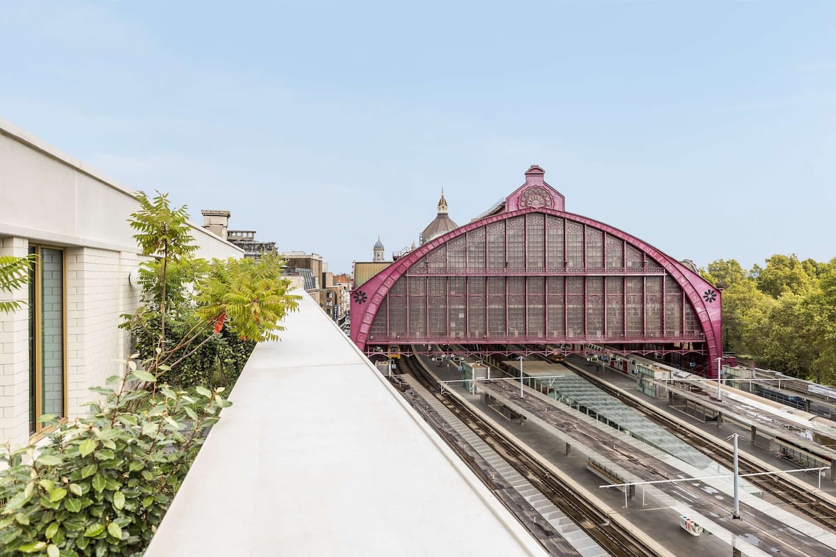 Une gare ferroviaire dotée d’une imposante structure en arc rose et de nombreuses voies ferrées.