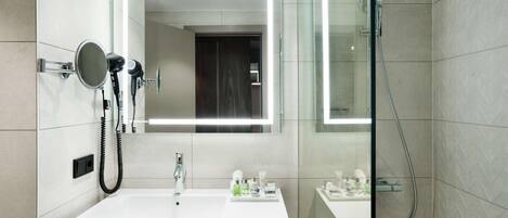 A modern bathroom with a large mirror, a white sink, and a shower.