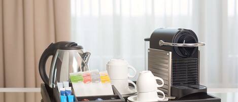 A coffee machine with a tray of coffee cups, a coffee pot, and coffee pods on a table.