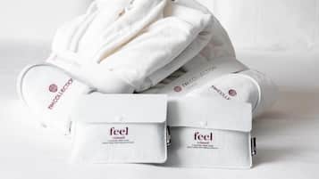 Un conjunto ordenado de toallas y albornoces blancos con el logo de 'feel' y el logo 'NH Collection' sobre una cama.