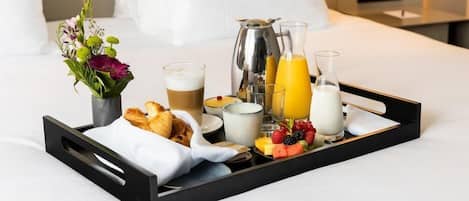 Ein Frühstücksbrett mit Croissants, Kaffee, Orangensaft, Milch und frischem Obst auf einem Bett.