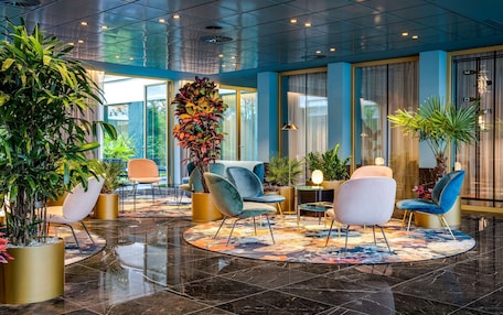 A lobby with a circular seating area, large potted plants, and a modern ceiling design.