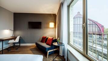 Quarto de hotel com cama, escrivaninha, sofá e televisão.