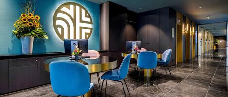 A modern hotel lobby with a reception desk, blue chairs, and a large decorative wall piece.