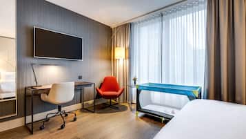 Een hotelkamer met een bed, een bureau met stoel, een televisie, een lamp en een raam met gordijnen.