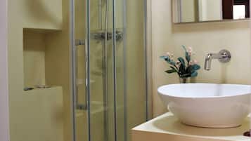 A bathroom with a glass-enclosed shower, a white sink with a vase of flowers, and a mirror above the sink.