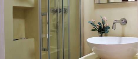 A bathroom with a glass-enclosed shower, a white sink with a vase of flowers, and a mirror above the sink.