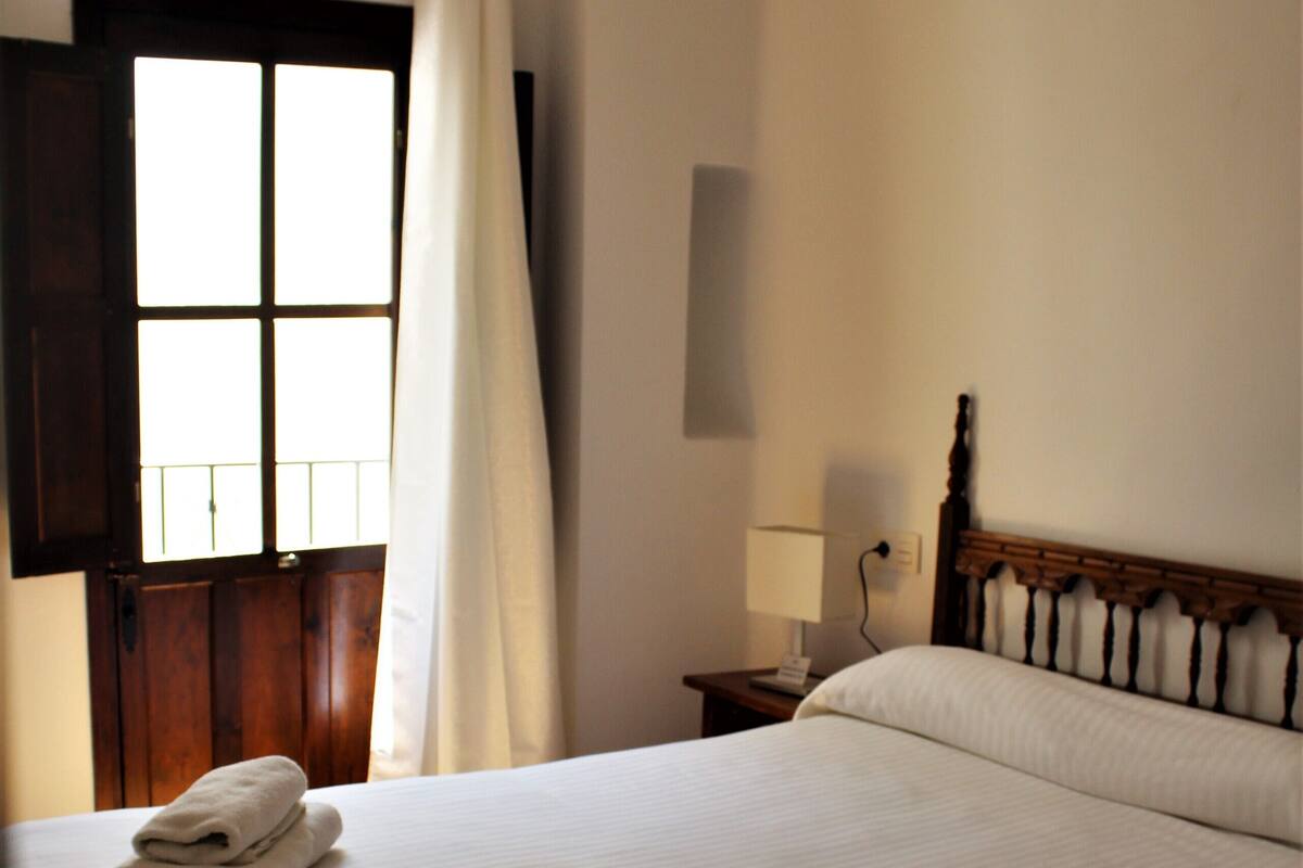 A hotel room with a large bed, a nightstand, a lamp, and a window with curtains.