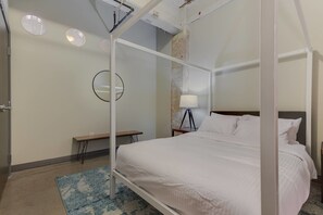 A four-poster bed with white bedding, a bedside table with a lamp, and a small bench.