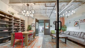 An office space with a wooden table, red chairs, a sofa, and shelves with various items. - Brand New Stunning Unit Downtown (Dallas)
