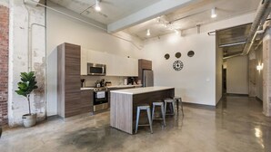 A modern kitchen with a central island, stainless steel appliances, and a brick accent wall. - Beautiful 3bd Unit in Perfect Downtown Location (Dallas)